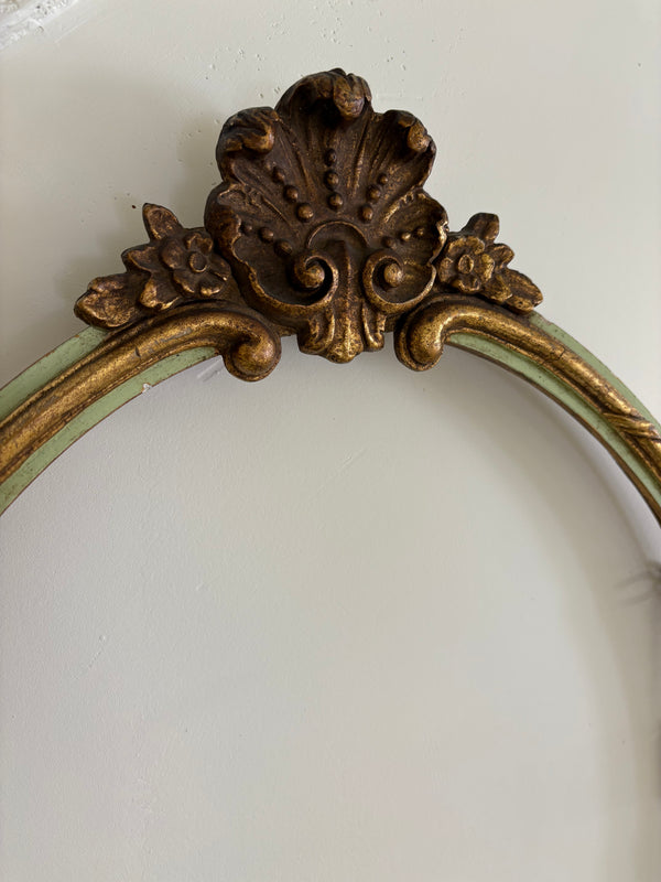 Oval gold gilded mirror with green trim.