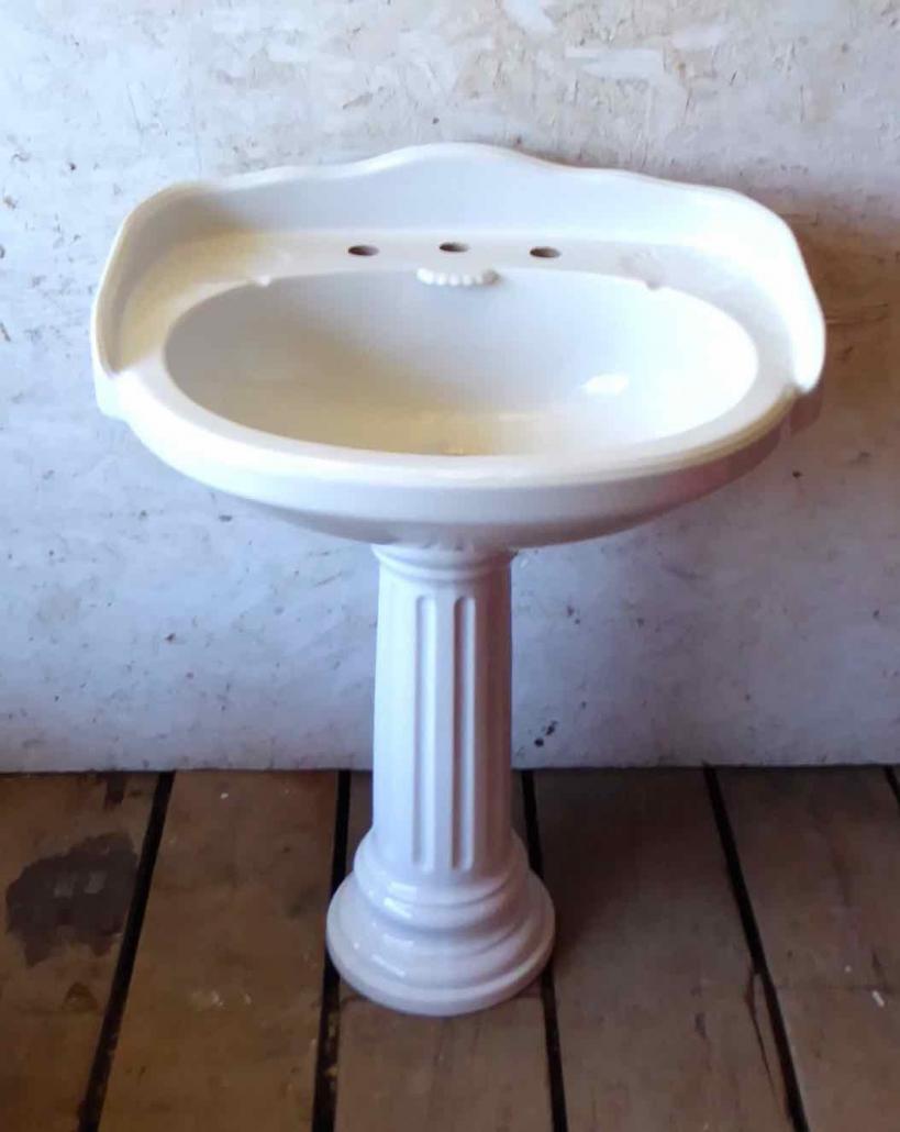 Antique porcelain pedestal bathroom sink with roman column motif pedestal and clamshell motif sink. Prop rental only