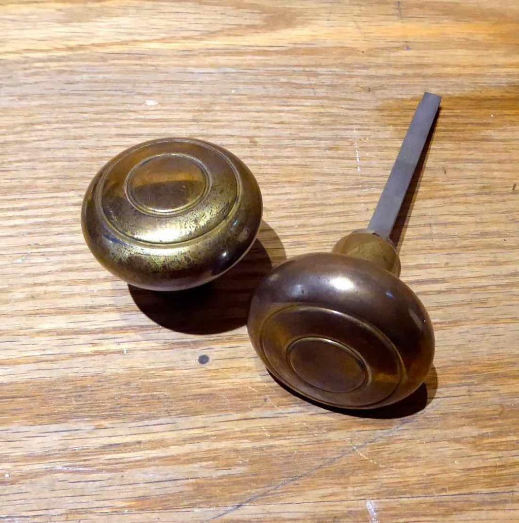 Closeup of doorknobs - Antique Art Deco stamped steel with remnant brass plating passage set. Set includes: remnant brass plated patterned doorknobs and remnant brass plated patterned backplates.