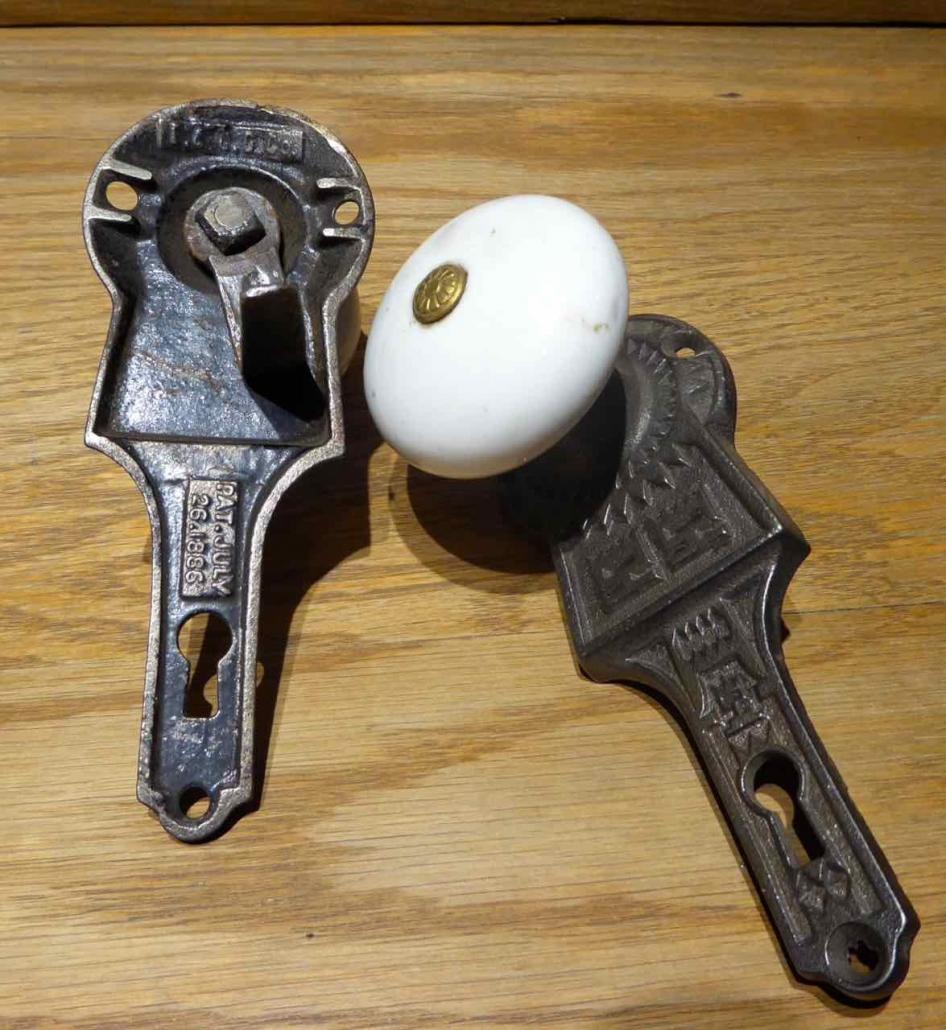 Closeup of doorknobs and patterned backplates - Original Victorian style cast iron passage set with porcelain door knobs and cast iron gravity lock. Gravity lock made by Gurney. Features porcelain doorknobs built into patterned backplates.