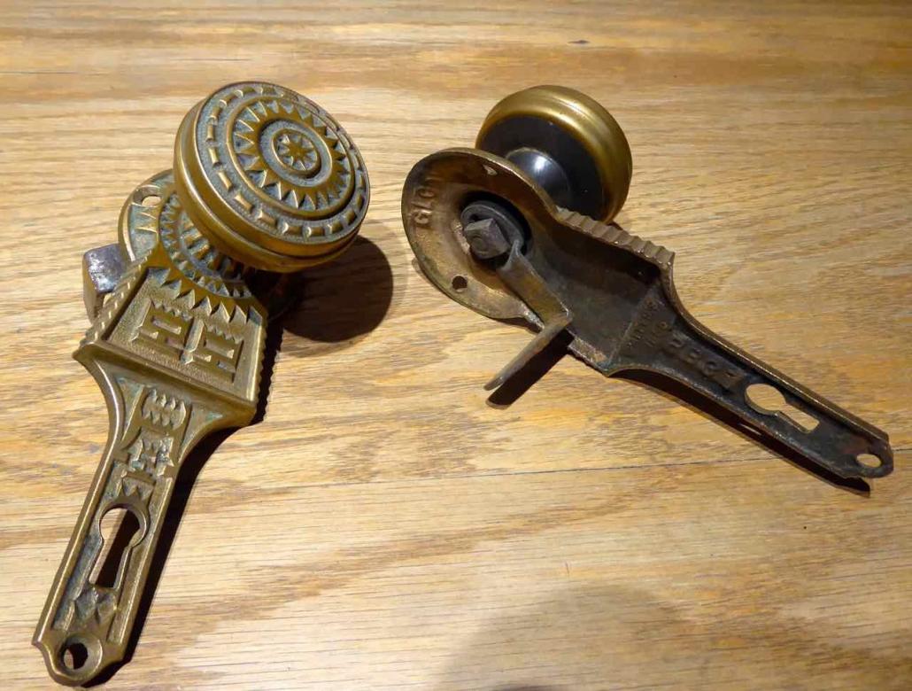 Closeup of doorknobs and backplates - Antique Victorian style cast iron passage set with solid brass doorknobs and cast iron gravity lock. Gravity lock made by Gurney. Features solid brass doorknobs built into patterned brass backplates.